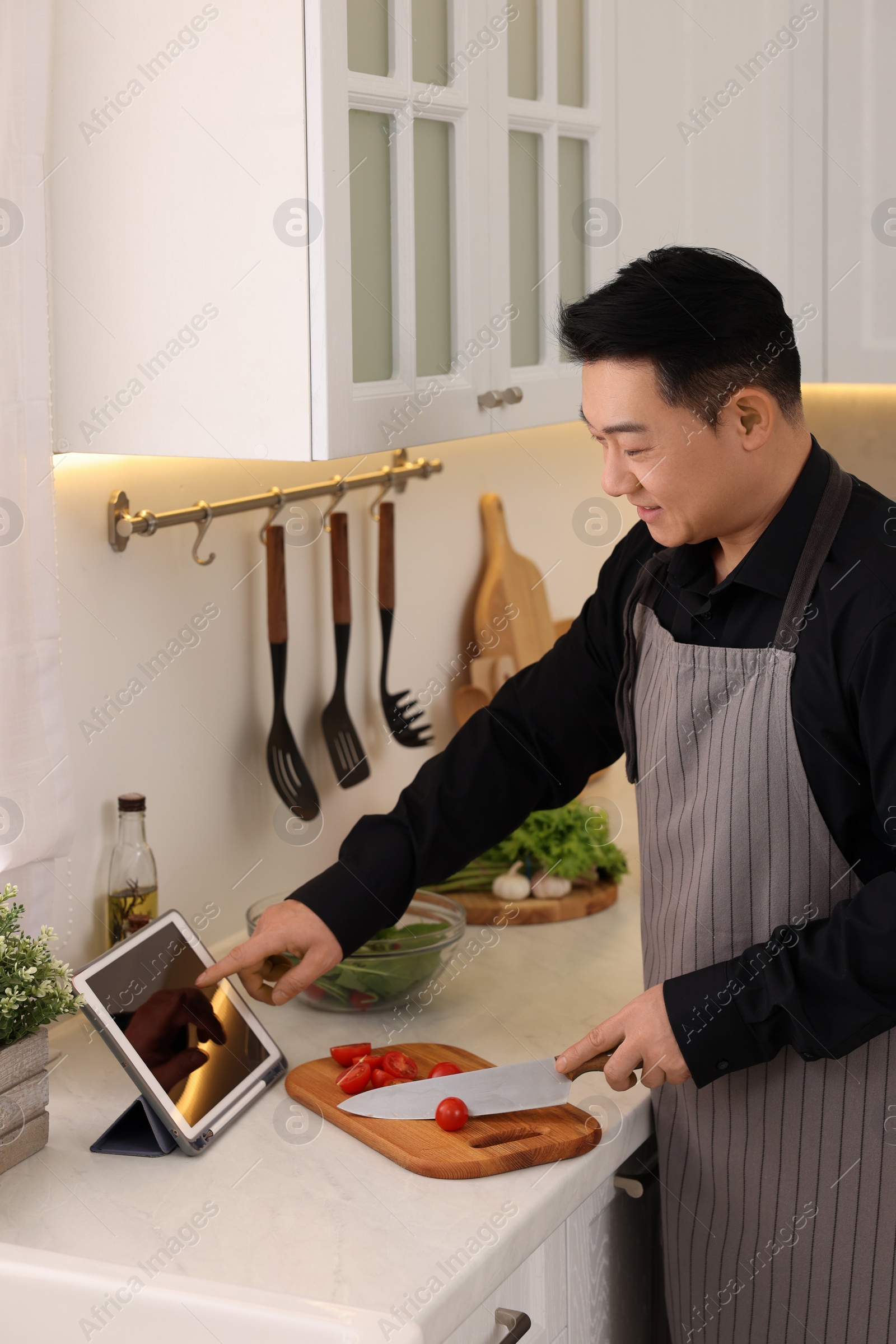 Photo of Man using tablet while cooking in kitchen