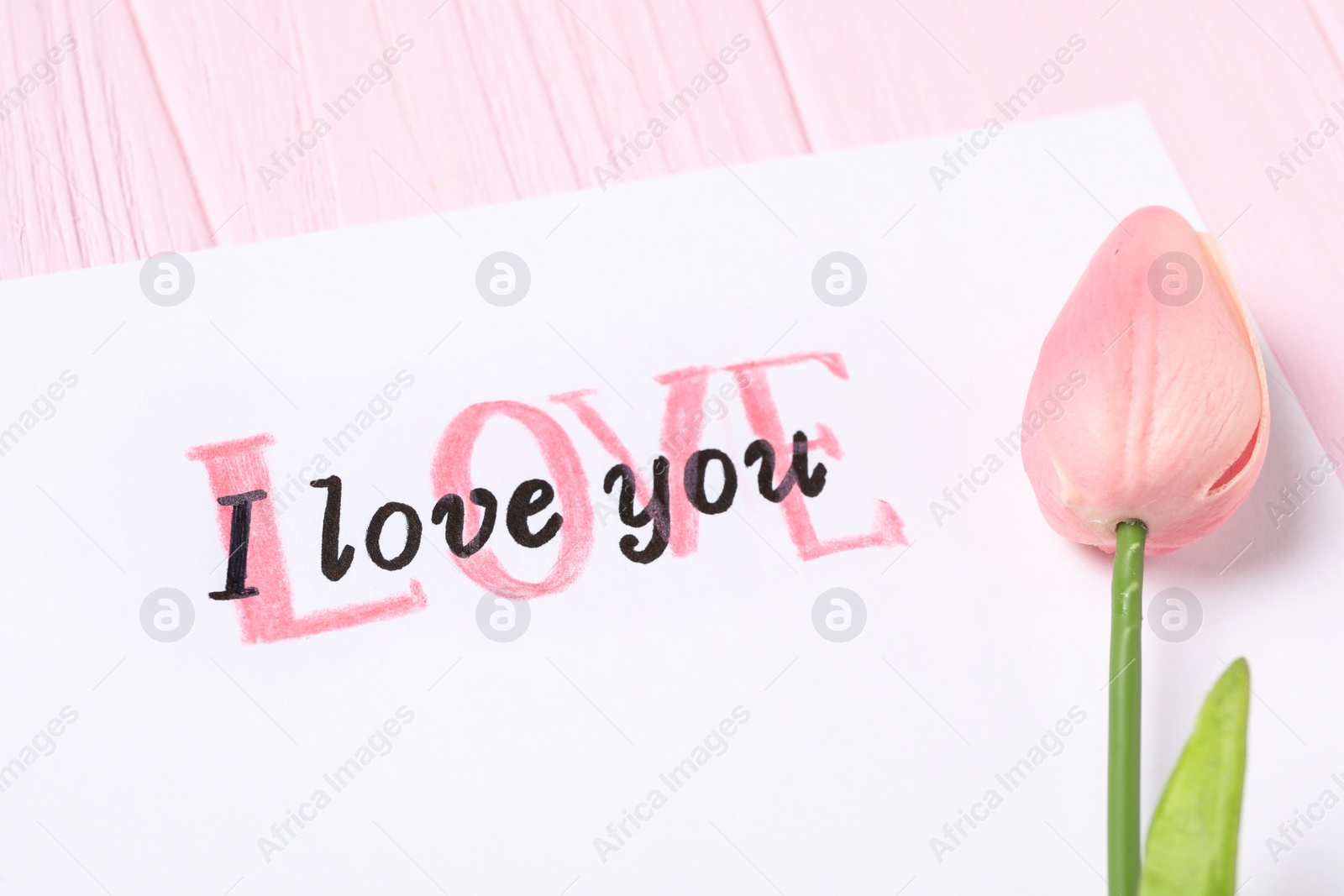 Photo of Card with text I Love You and tulip on pink wooden background, closeup