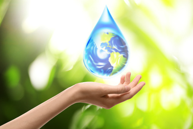 Image of Woman holding icon of Earth in water drop on blurred green background, closeup. Ecology concept