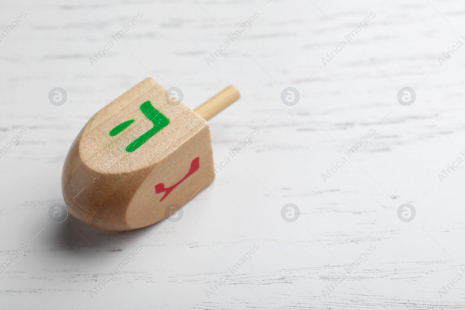 Photo of Hanukkah traditional dreidel on white wooden background, closeup. Space for text