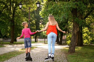 Photo of Mother and son roller skating in summer park, back view