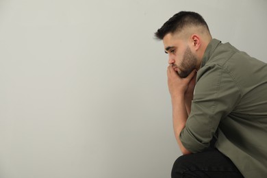 Photo of Sad man sitting near light grey wall. Space for text