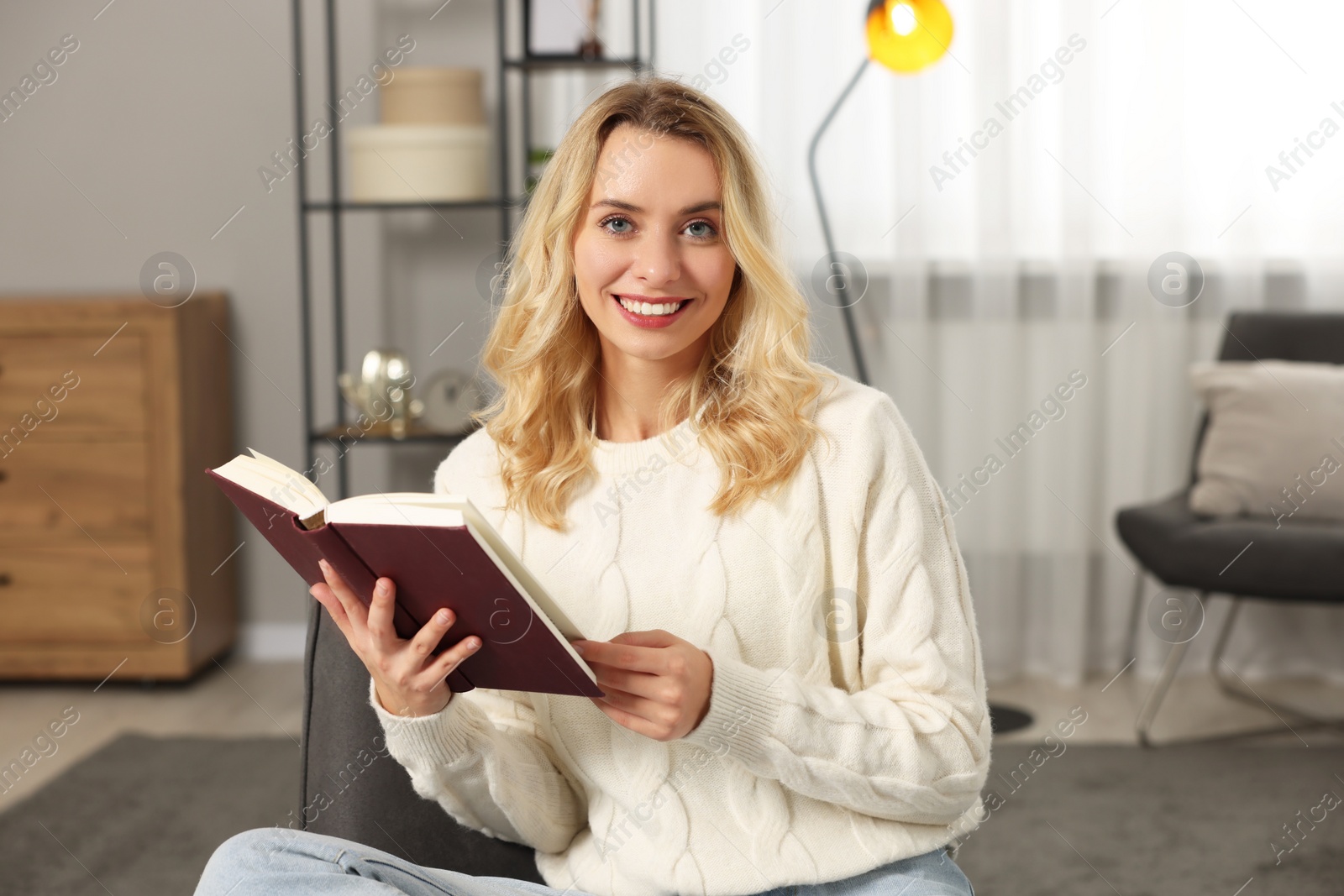 Photo of Happy woman in stylish warm sweater reading book at home