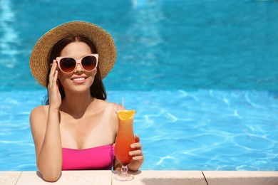 Beautiful young woman with cocktail in swimming pool. Space for text