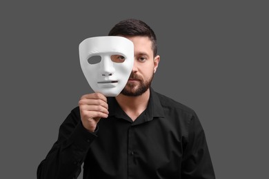 Multiple personality concept. Man covering face with mask on grey background