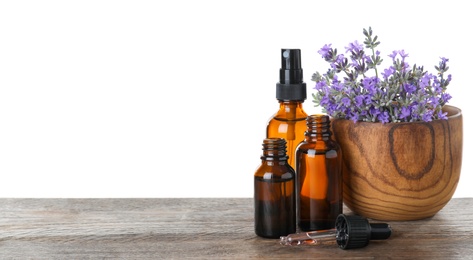 Bottles of essential oil and bowl with lavender flowers on wooden table against white background