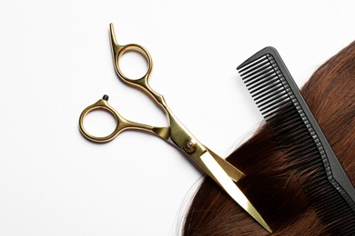 Photo of Professional hairdresser scissors and comb with brown hair strand on white background, flat lay