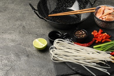 Photo of Different products and wok with chopsticks on dark textured table, closeup. Space for text