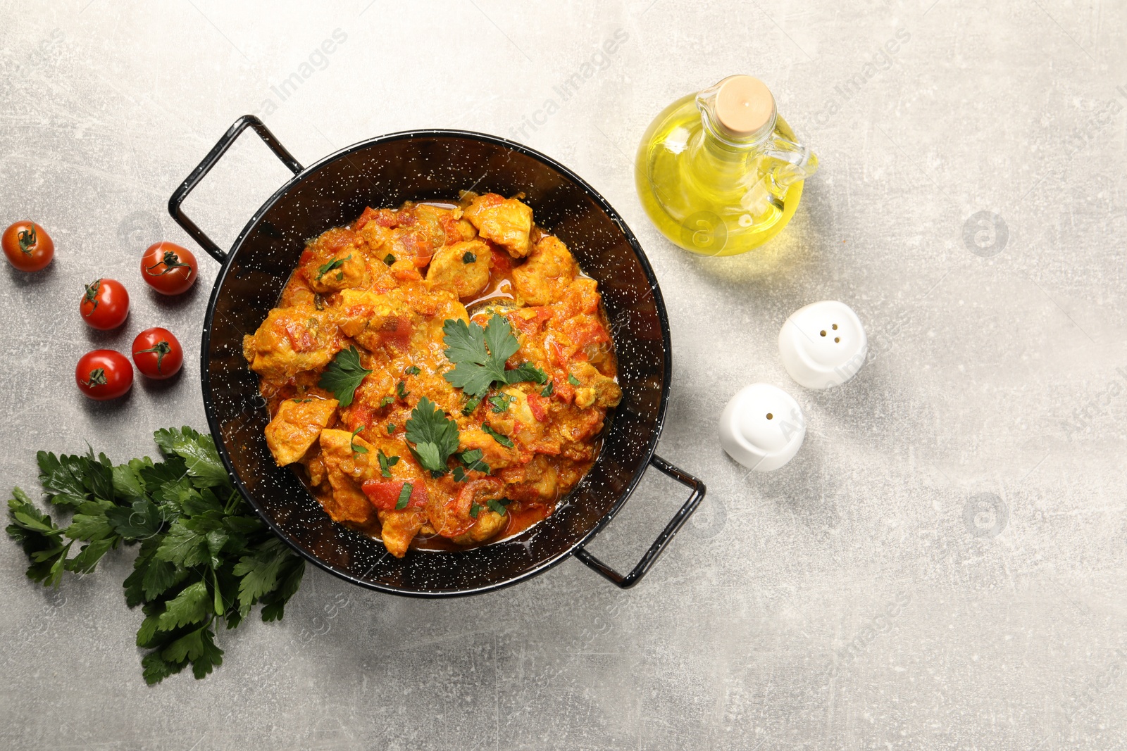 Photo of Delicious chicken curry in frying pan, parsley, tomatoes and oil on light grey table, flat lay. Space for text