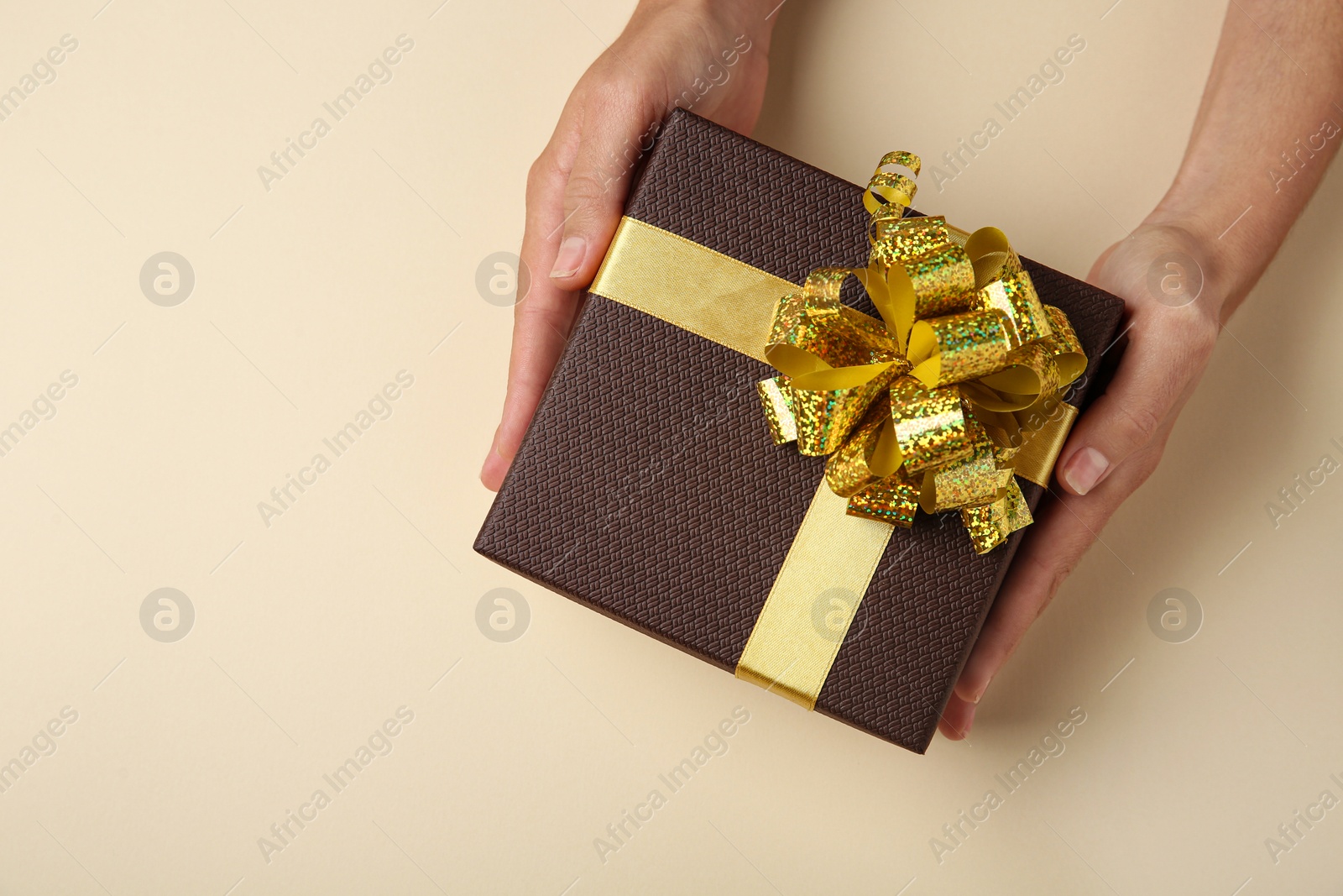 Photo of Woman holding beautiful gift box on beige background, top view. Space for text