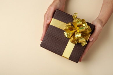 Photo of Woman holding beautiful gift box on beige background, top view. Space for text