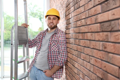 Young working man with ladder near brick wall. Space for text