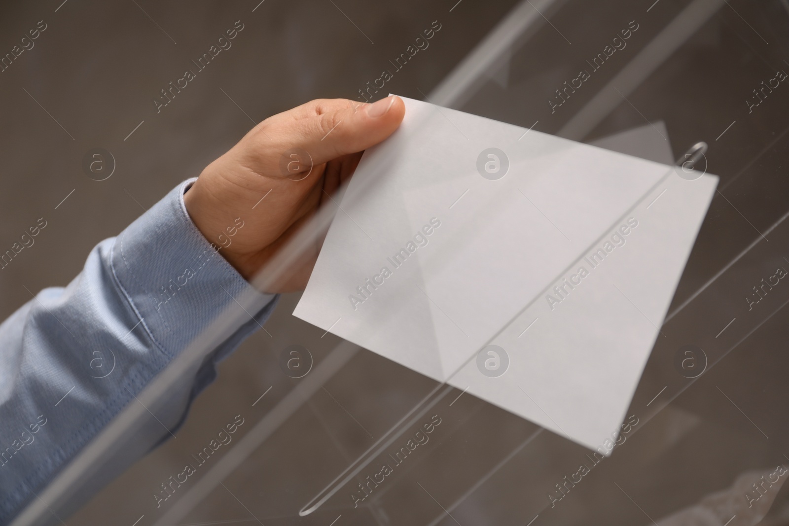 Photo of Man putting his vote into ballot box on color background, closeup