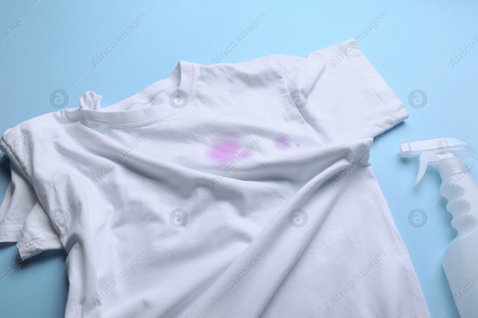 Photo of White shirt with purple stains and detergent on light blue background, above view