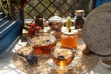 Aromatic tea with different dry plants and honey on white wooden table near window