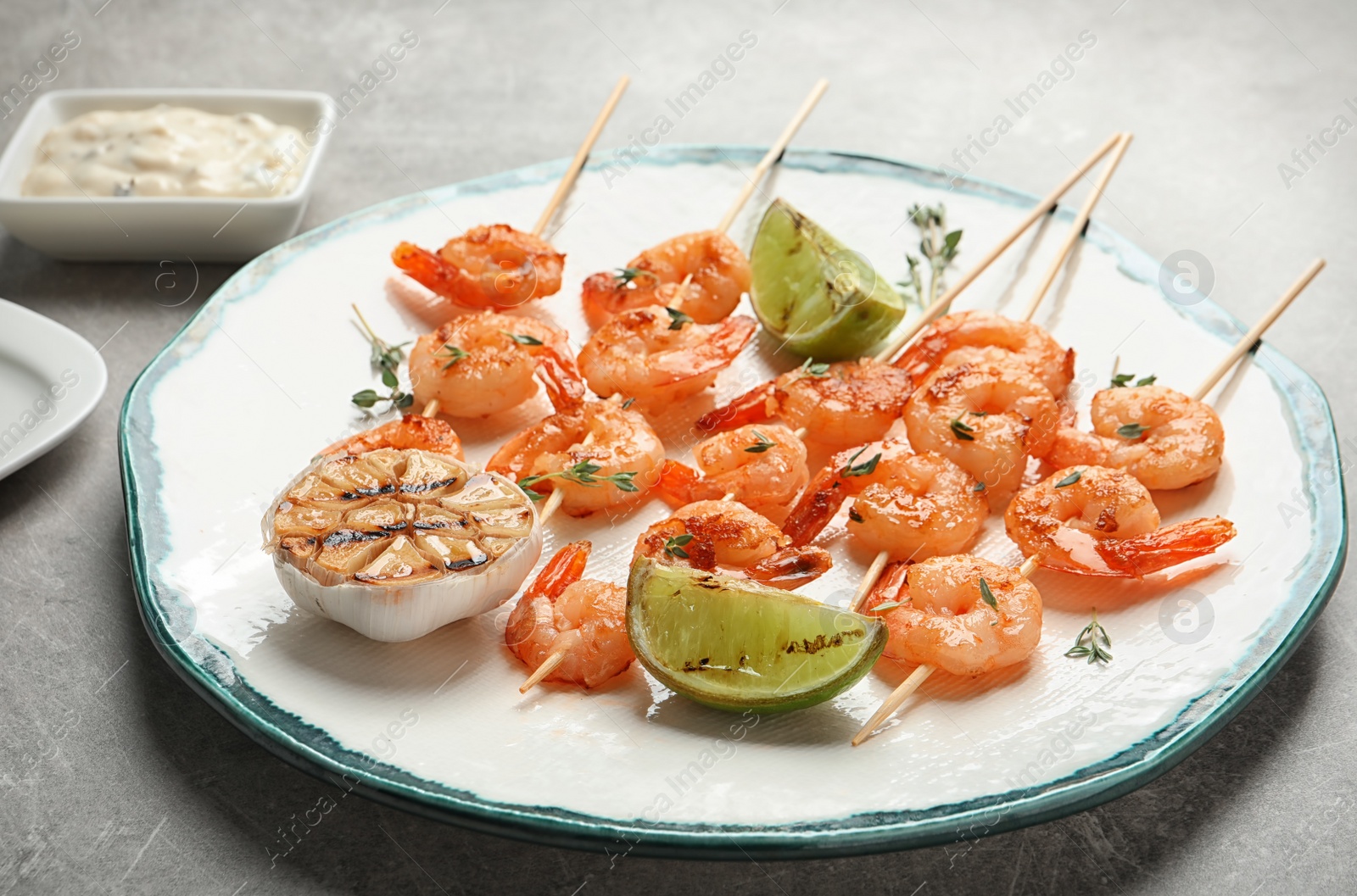 Photo of Plate with delicious fried shrimp skewers and lime on grey background