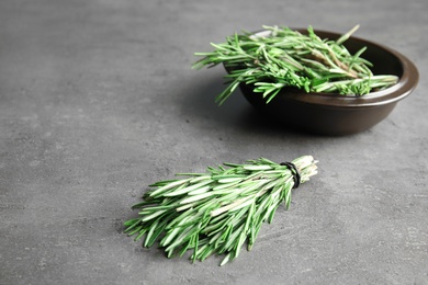 Bunch and bowl with fresh rosemary on grey table