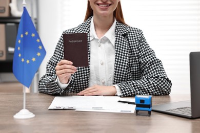 Immigration to European Union. Smiling embassy worker with passport and documents at wooden table in office, closeup