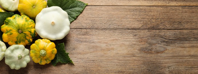 Fresh ripe pattypan squashes with leaves on wooden table, flat lay with space for text. Banner design