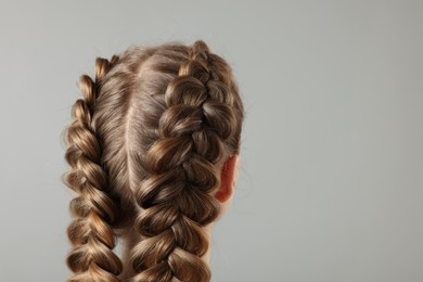 Photo of Woman with braided hair on grey background, back view. Space for text