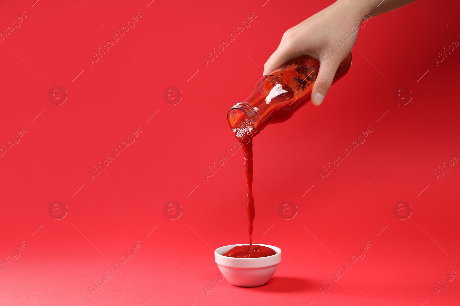 Photo of Woman pouring tasty ketchup from bottle into bowl on red background, closeup. Space for text