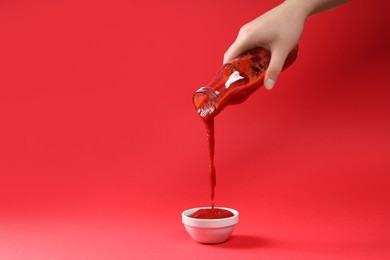 Photo of Woman pouring tasty ketchup from bottle into bowl on red background, closeup. Space for text