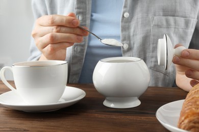 Photo of Woman adding sugar into cup of tea at wooden table, closeup