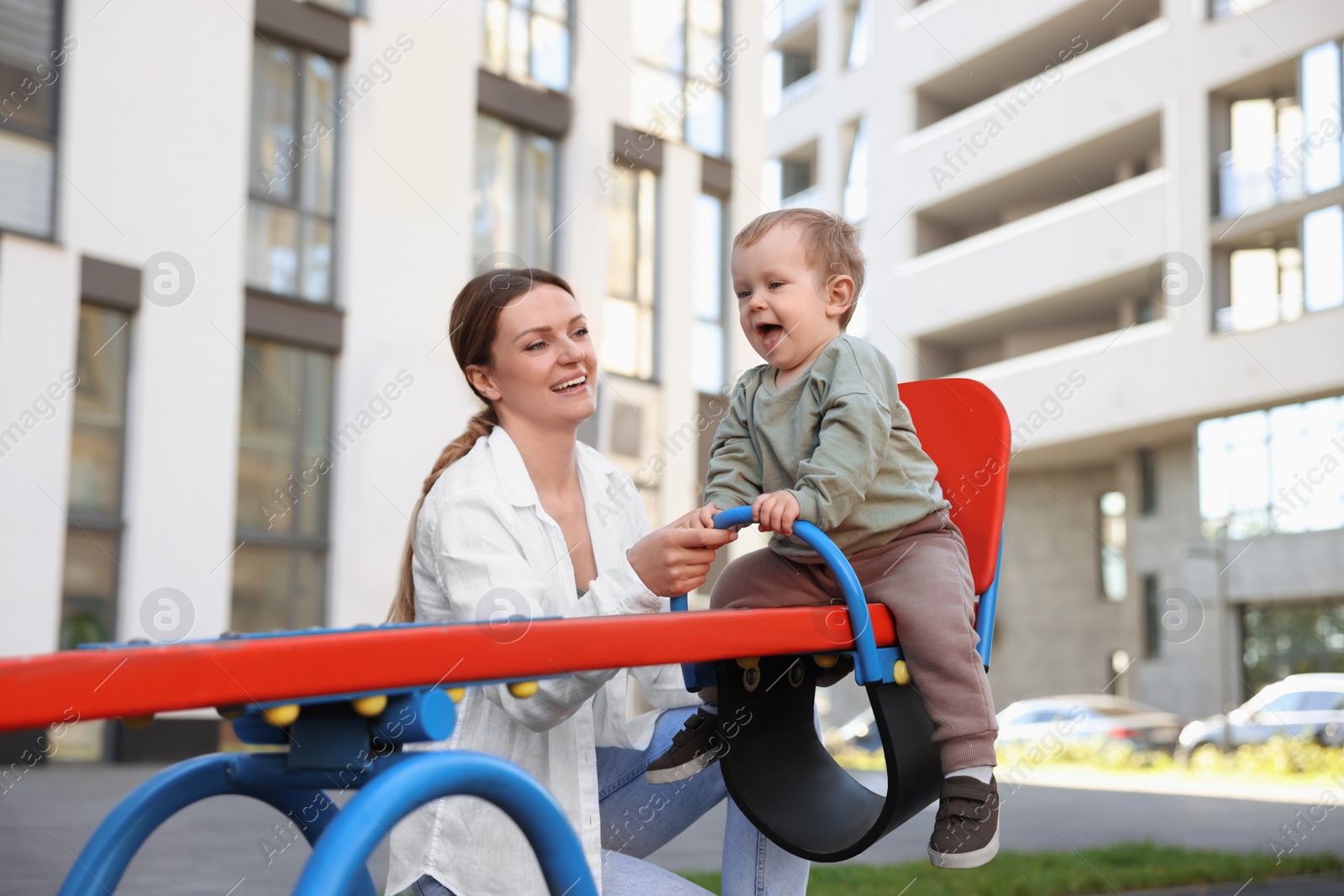 Photo of Happy nanny and cute little boy on seesaw outdoors