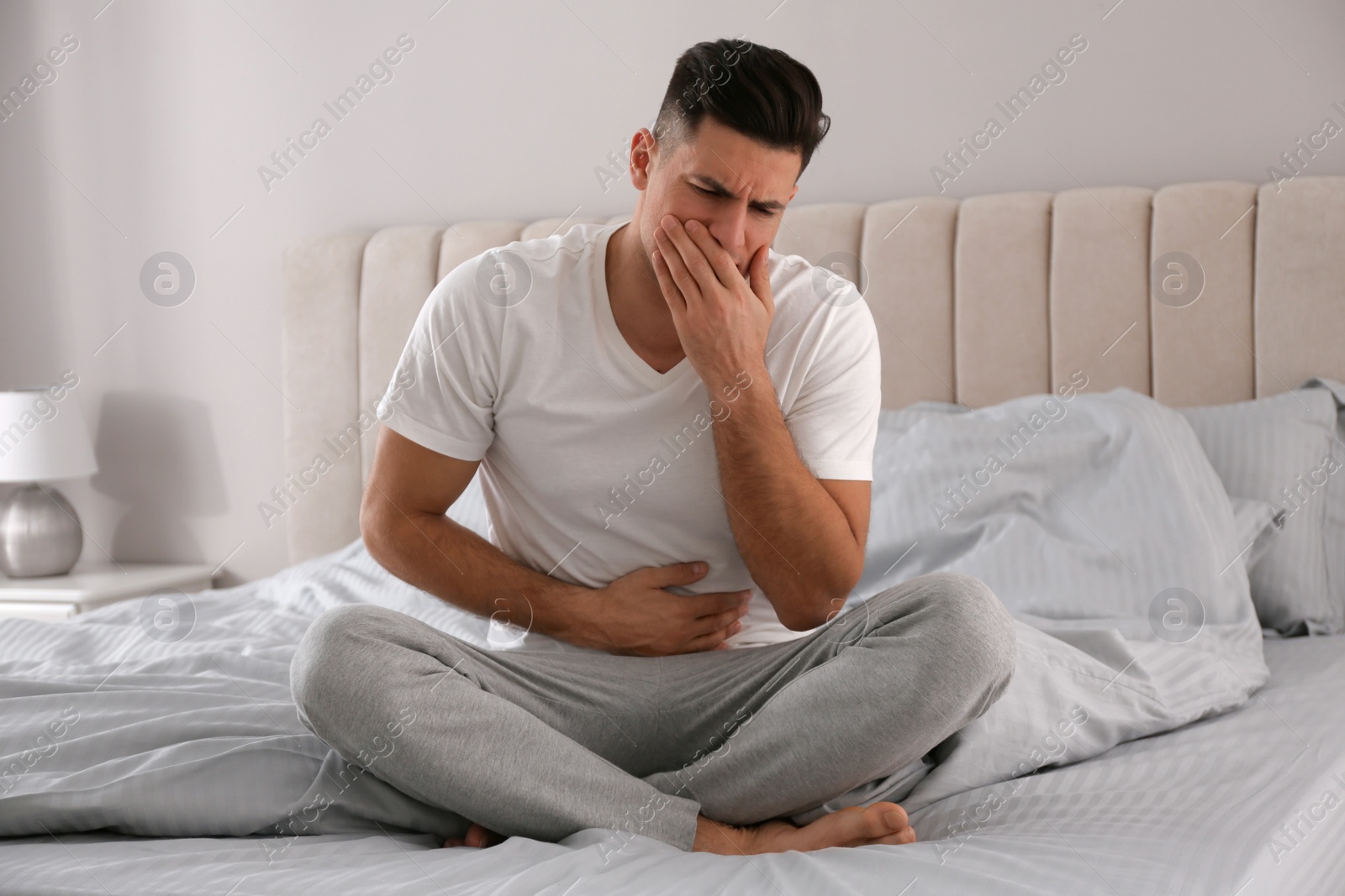 Photo of Man suffering from nausea on bed at home. Food poisoning