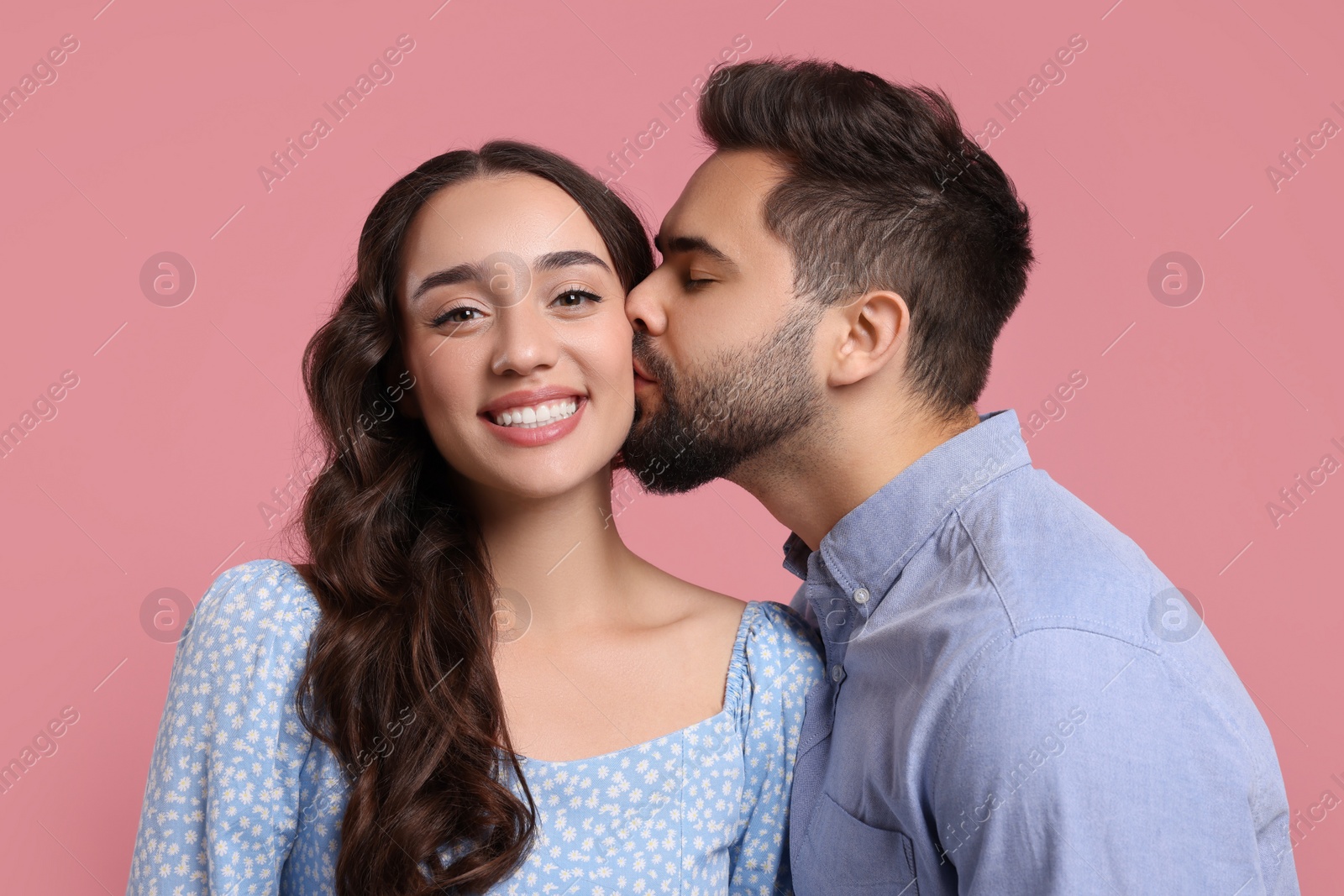 Photo of Man kissing his smiling girlfriend on pink background