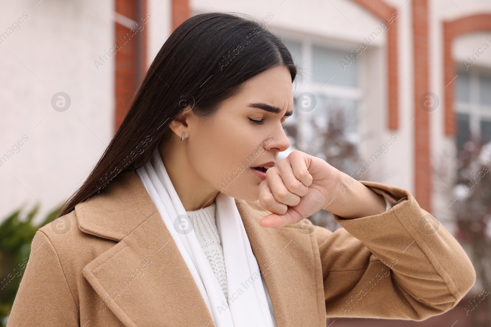 Photo of Woman in coat coughing outdoors. Cold symptoms