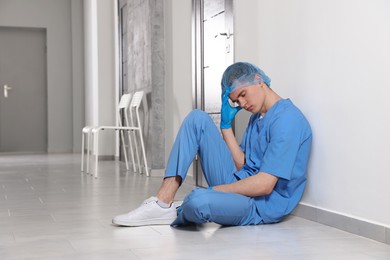Exhausted doctor sitting near grey wall in hospital hallway