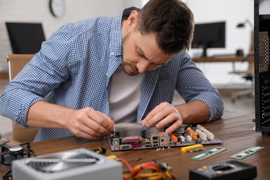 Photo of Male technician repairing motherboard at table indoors