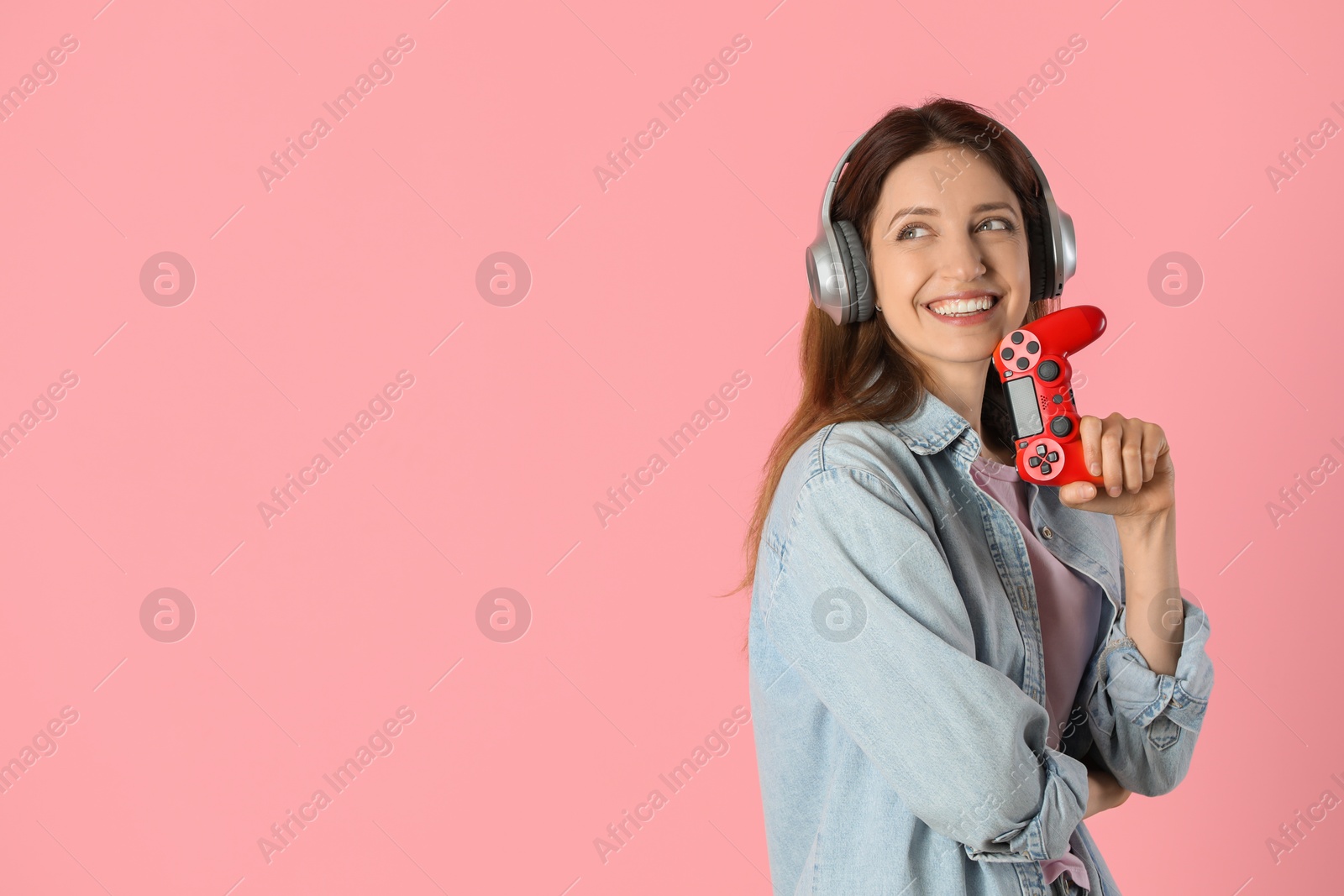 Photo of Happy woman in headphones with game controller on pink background. Space for text