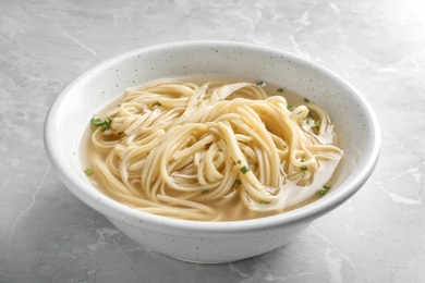 Photo of Bowl of tasty noodles with broth on table, closeup