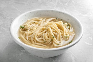 Bowl of tasty noodles with broth on table, closeup