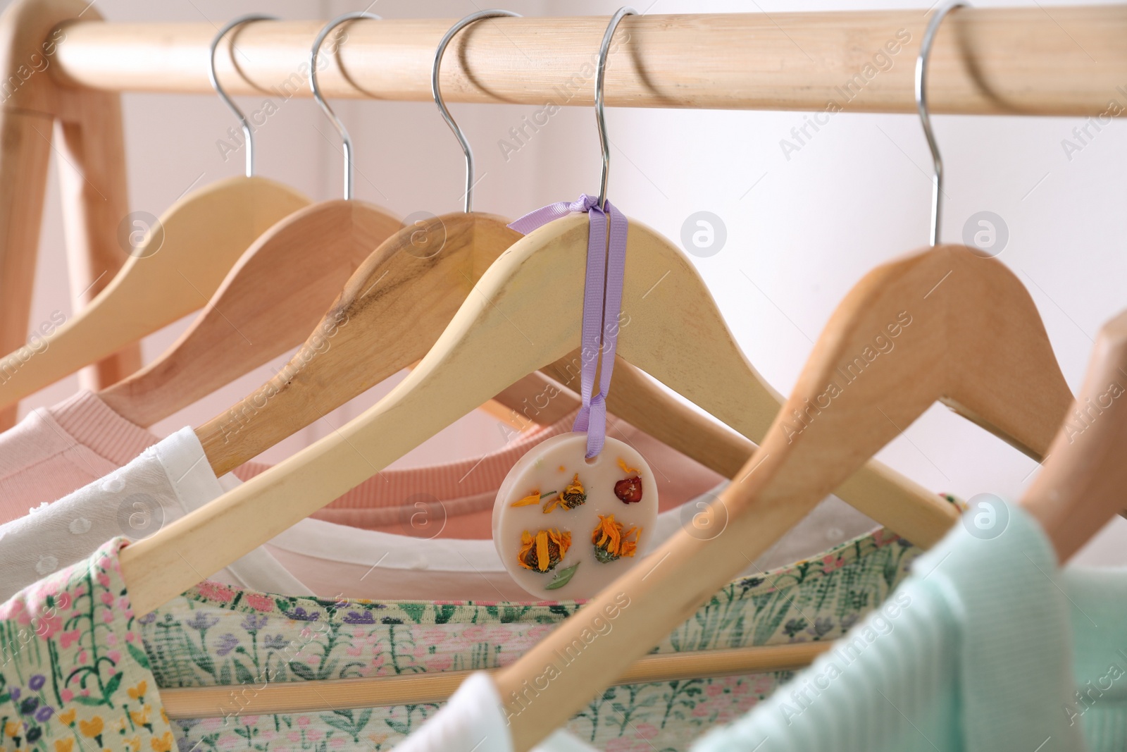 Photo of Beautiful scented wax sachet and clothes hanging on wooden rack indoors, closeup