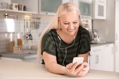 Mature woman listening to music on mobile phone at home