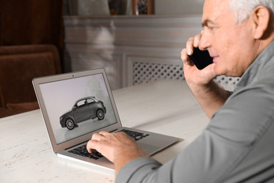 Photo of Man using laptop to buy car at table indoors