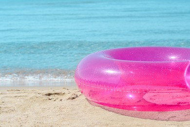 Photo of Bright inflatable ring on sandy beach near sea, closeup. Space for text