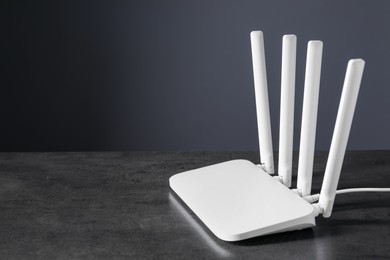 Photo of New stylish Wi-Fi router on black textured table. Space for text
