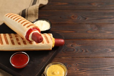 Photo of Delicious french hot dogs and dip sauces on wooden table. Space for text
