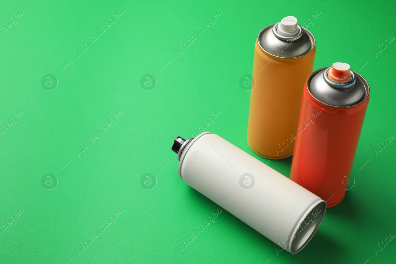 Photo of Cans of different spray paints on green background, space for text. Graffiti supplies
