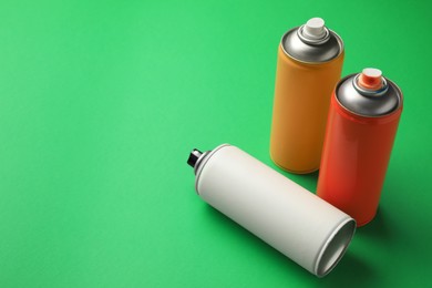 Photo of Cans of different spray paints on green background, space for text. Graffiti supplies