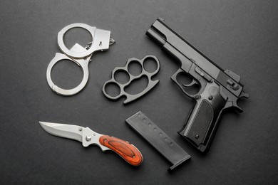 Brass knuckles, gun, knife and handcuffs on black background, flat lay