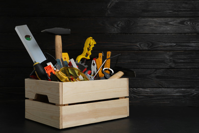 Photo of Wooden crate with different carpenter's tools on black table. Space for text