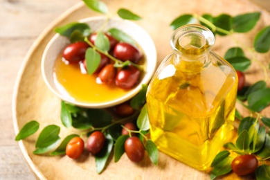 Glass bottle with jojoba oil and seeds on wooden table