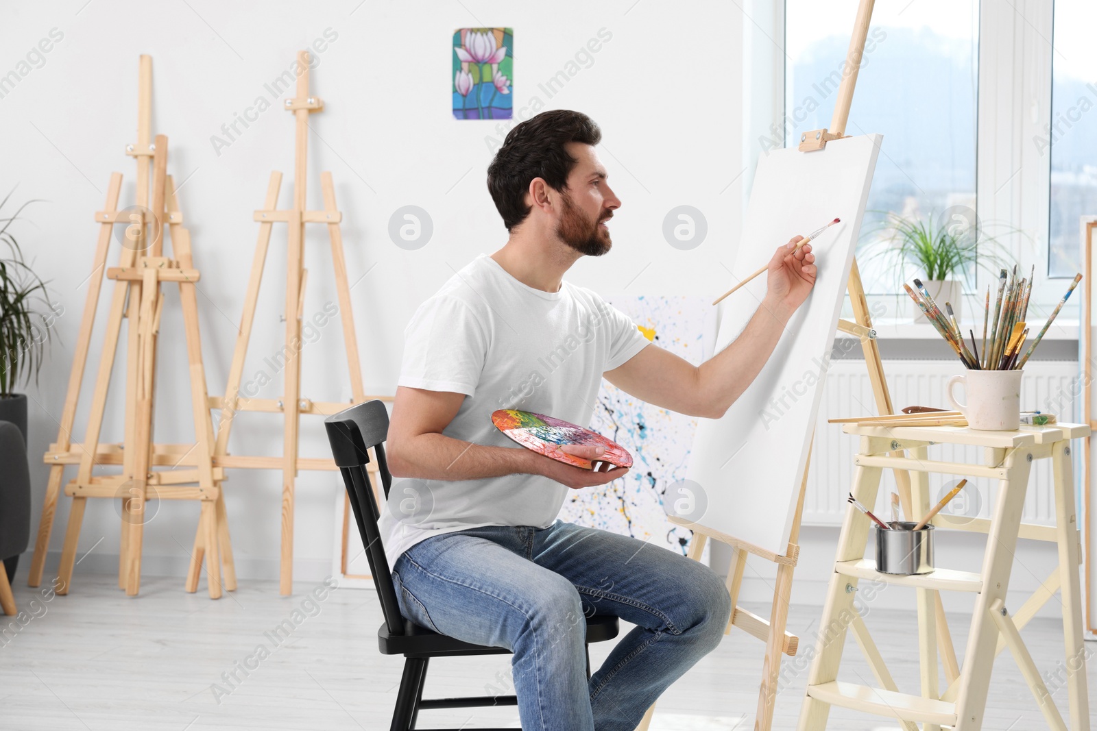 Photo of Man painting in studio. Using easel to hold canvas