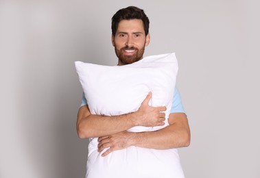 Smiling handsome man hugging soft pillow on light grey background