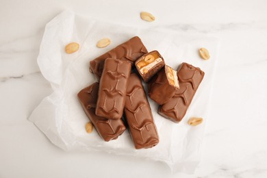 Photo of Chocolate bars with caramel, nuts and nougat on white marble table, flat lay